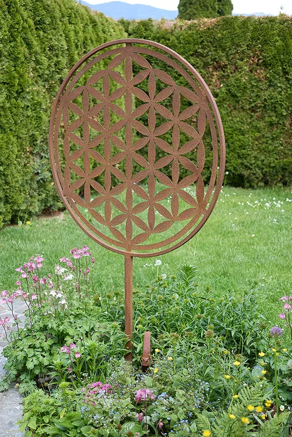 Gartenskulptur mit geometrischem Muster auf Rasen, umgeben von blühenden Pflanzen.