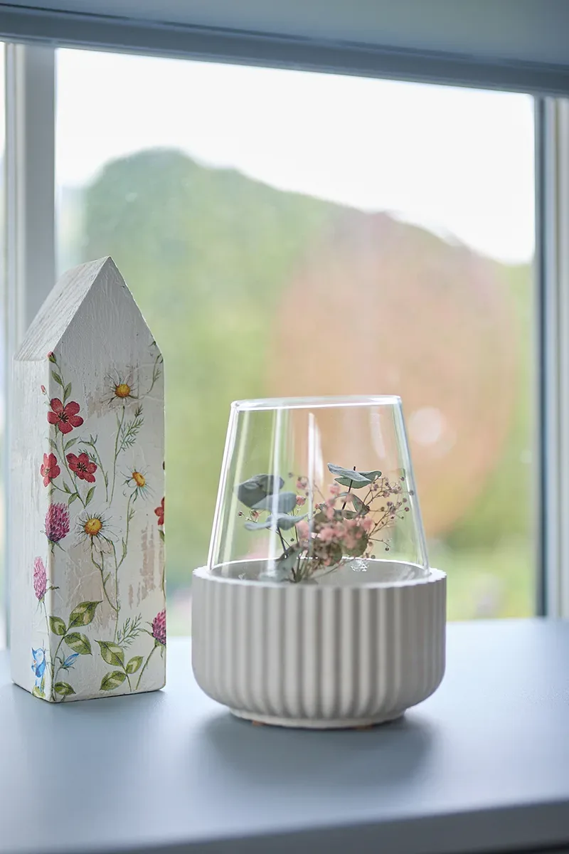 Dekorative Glasglocke mit Vögeln und Blumen auf Fensterbank.