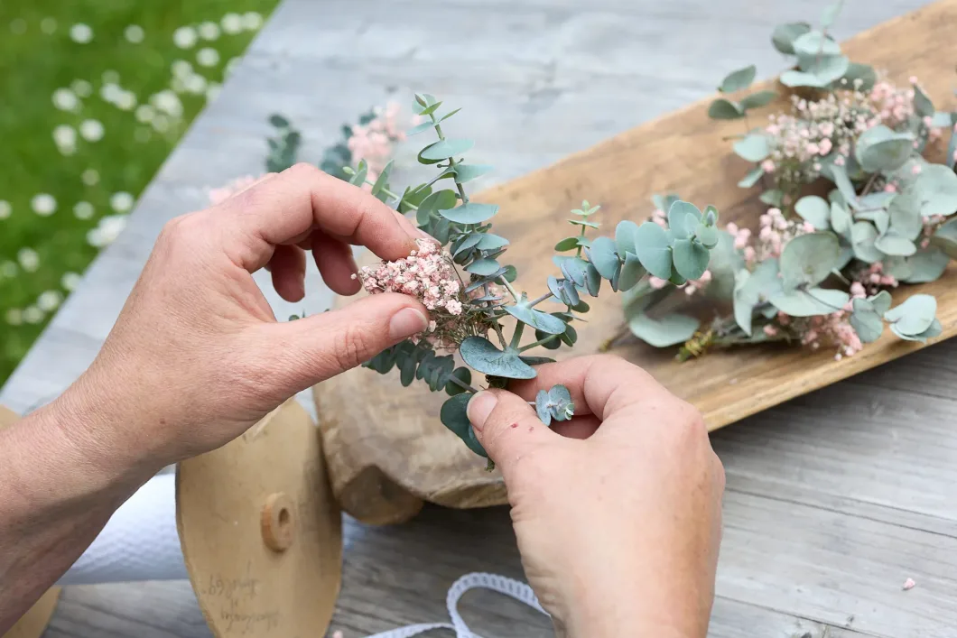 Hände gestalten Gesteck mit Eukalyptus und rosa Blüten auf Holztisch. – handgearbeitete Deko Trieben